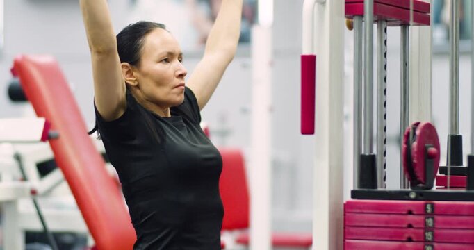 Caucasian woman doing exercise on a lat machine in the gym. Pulldown reps during gym workout session. Woman performs lat pulldown reps on the machine, focusing on back muscle strength.
