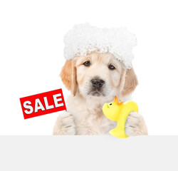 Cute Golden Retriever puppy with soap foam on it head holds rubber duck and shows signboard with labeled "sale" above blank white banner. isolated on white background