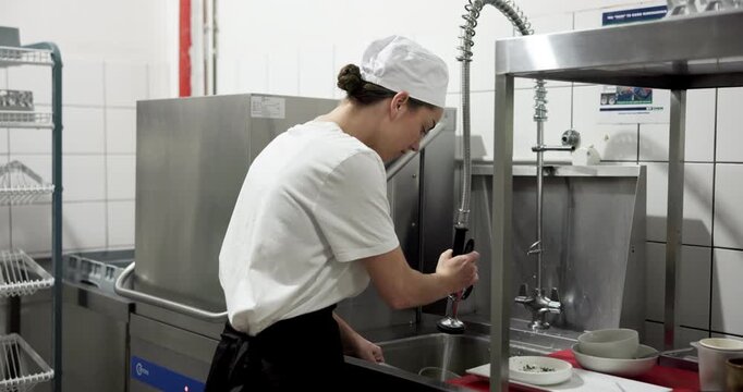 Washing dishes, sanitary and restaurant with woman in kitchen as dishwasher, cleaning and hospitality. Scullery worker, hygiene and bacteria protection with person in cafe for food safety policy