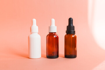 Different serum cosmetic bottles, white and dark brown dropper bottle container and packaging skincare product. studio pastel light background.