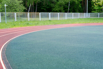 Curved running track with vibrant red lines, surrounded by lush green grass and a white fence, creating an inviting atmosphere for athletic activities and outdoor sports
