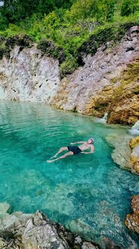 Person floating in turquoise waters surrounded by rocky cliffs and forest in JABA sulfur lagoon in Tanjay, Negros Oriental, Philippines