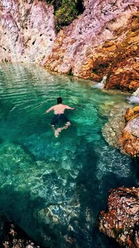 Overhead view of a man wading into the ethereal clear water of the JABA sulfur lagoon, a hidden tourist attraction in Amlan, Negros Oriental, Philippines
