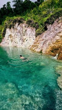 A man leisurely swimming in emerald water with rocky limestone cliffs and forest creating a serene escape in JABA sulfur lagoon in Tanjay, Philippines