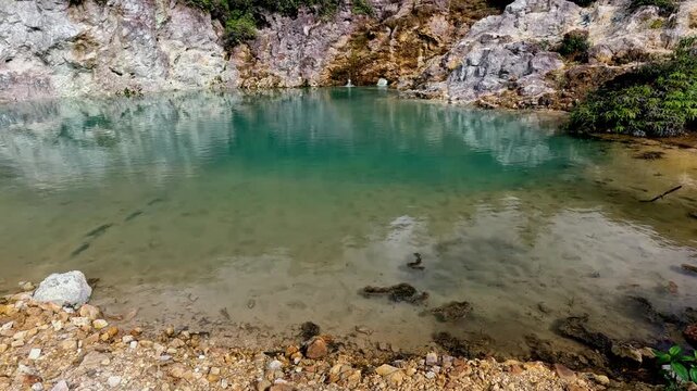 Tilt up to reveal the pool of blue clear water and rugged white lime and red wall of rocks in the JABA sulfur lagoon. Tanjay, Negros Oriental, Philippines