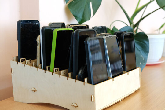 Schoolchildren's mobile phones stored in a wooden box on a classroom desk, illustrating the ban on devices during educational activities and promoting focus on learning