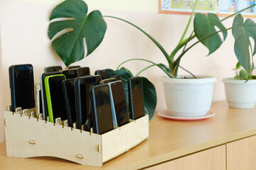 Schoolchildren's mobile phones neatly organized in a wooden box on a classroom shelf, emphasizing the ban on devices during educational activities and promoting focus on learning