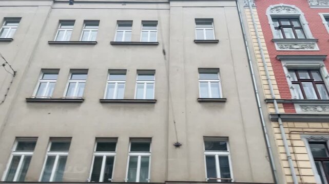 colorful facades lining narrow alley. vertical street view of mixed historic exteriors with plaster textures, ornate cornices and windows, overhead wires and muted sky, Video taken on mobile devicr.