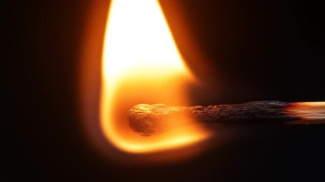 Close-up of a lit matchstick with flame against a dark backdrop; glowing orange fire