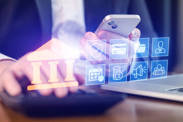 Business person uses smartphone and laptop for online banking tasks in an office setting during daytime hours