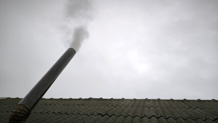 old metal chimney on the roof with grey smoke coming out