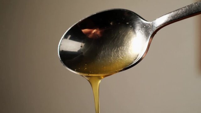 Close-up of a silver spoon holding golden honey syrup slowly dripping in soft natural light with copy space