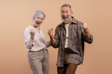 Senior couple feeling excited and winning, celebrating success with happy expressions