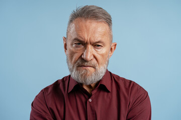 Obraz premium Senior man frowning, expressing anger and disapproval with a serious face
