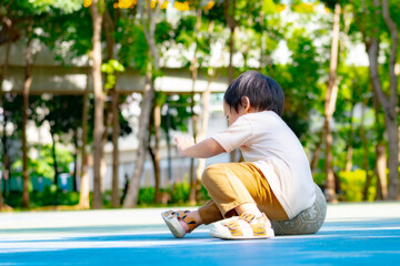 young Asian boy sitting on a soccer ball in a green park during a sunny day. Concept of active lifestyle, childhood play, physical development, and outdoor recreation for toddlers.