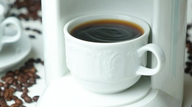 Close-up of fresh hot coffee dripping from a white machine into a cup slow motion
