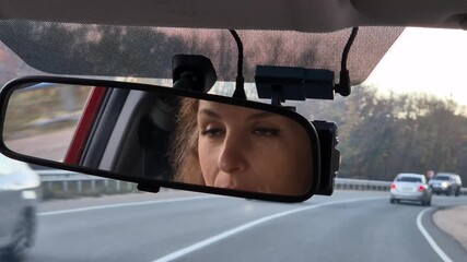 Driving Woman Rearview Mirror reflection on the road while traveling during an autumn day.