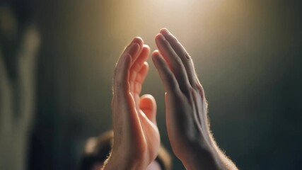 Close-up of hands joining together in prayer or meditation, illuminated by a soft, warm light from above, creating a serene and spiritual atmosphere.