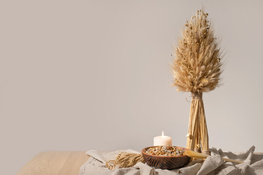 Traditional Christmas holiday celebration attributes in Ukraine. Didukh, sheaf of wheat and kutia, ritual dish on plate, on wooden table with linen, empty neutral beige wall background, copy space
