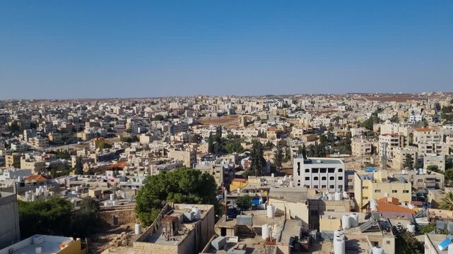 Panoramic view of Madaba, Jordan, as early evening sunlight bathes rooftops, with the city sprawling over rolling hills and fading into the distant horizon
