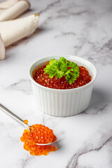 Red caviar bowl and spoon on marble with beige napkin