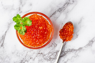Bowl of red caviar with parsley and spoon on marble