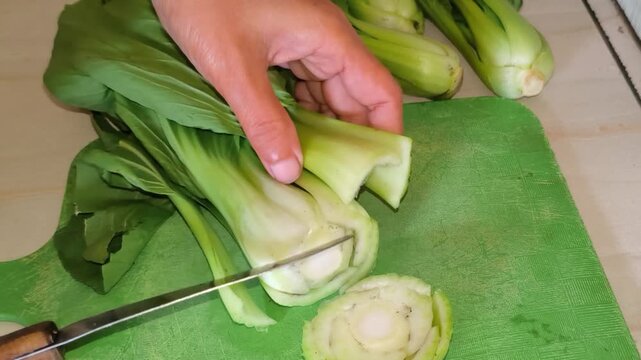 Close-up of hand cutting fresh green bok choy on a green cutting board with a knife.