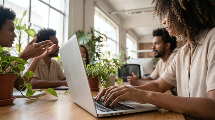 Diverse team collaborating on laptop in modern office space with plants
