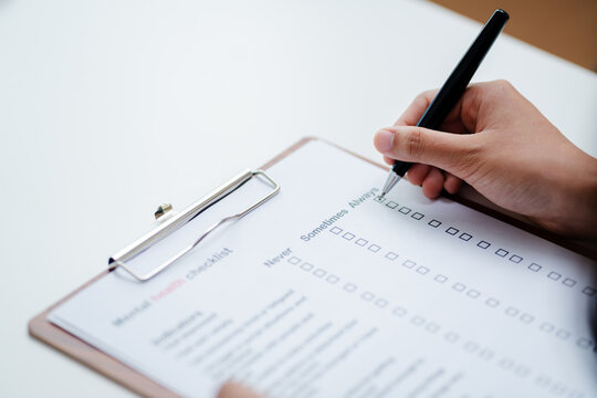 Person filling mental health checklist on clipboard with pen, psychological assessment, self evaluation, healthcare screening and wellbeing awareness concept.