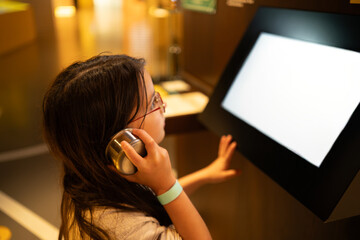 Curious teenage girl in glasses using headphones in museum, learning and discovery concept