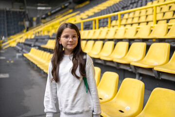 Smiling teenage girl on empty football stadium during excursion, travel education and fun concept