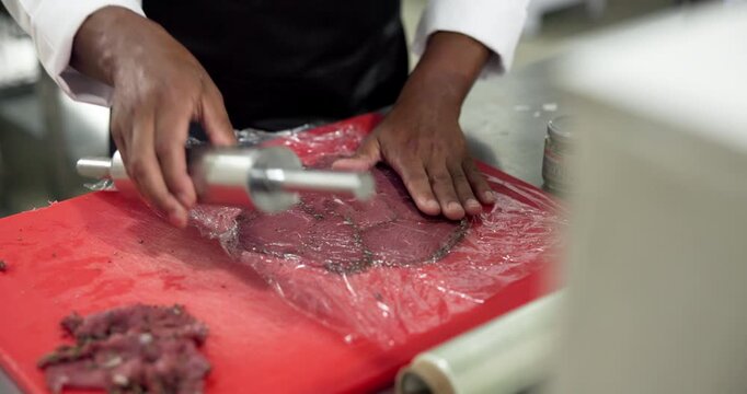 Hands, chef or flatten meat in restaurant to tenderize, enhance flavor or meal prep in food industry. Hospitality, person and rolling pin on steak in kitchen for easy searing, seasoning and cooking