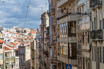 Telephoto view of crowded apartment building facades in Lisbon, Portugal, featuring many balconies, windows, and traditional red city rooftops.