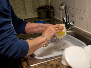 Older person washing dishes by hand in a sink, a common household chore in a typical kitchen setting