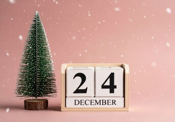 Miniature christmas tree with a wooden block calendar showing december 24th, with falling snow