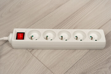 white grounded power strip with safety switch for home electrical protection, secure five-outlet extension cord on grey wooden floor for safe office energy supply