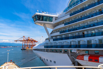 Cruise ship docking in vancouver harbor with cargo cranes in background