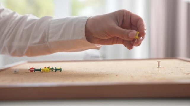 Hand Arranging Colorful Pushpins on Corkboard Surface