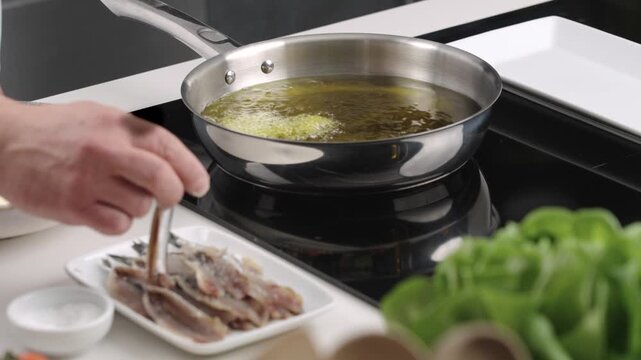 A man fry anchovies in a pan with oil. Cooking process on the stove. 
