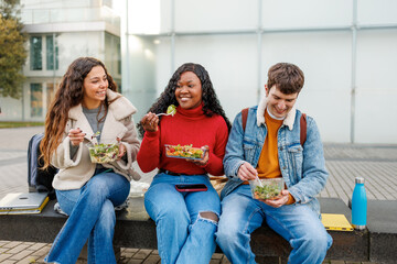 Students enjoying a healthy takeaway salad lunch together while sitting on a bench