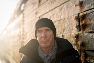 Man in beanie and scarf stands by weathered wall
