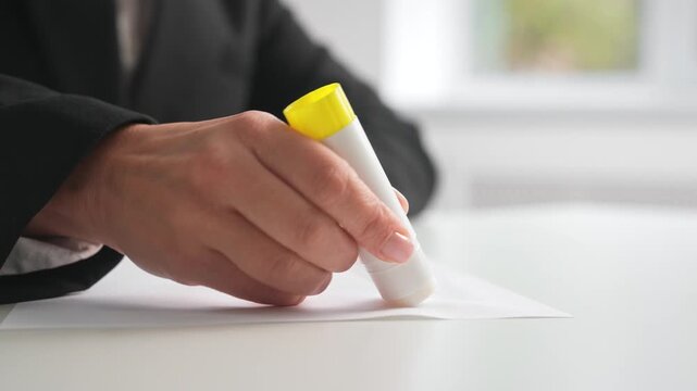 Hand Applying Glue Stick to White Paper on Desk