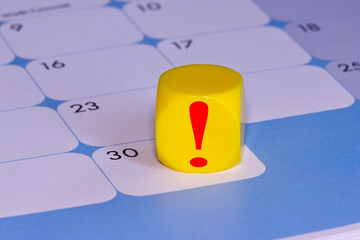 A red exclamation point on a yellow block placed on the 30th day of the month on a calendar,...
