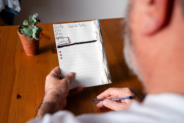 Ein &auml;lterer Mann sitzt an einem Holztisch und h&auml;lt ein offenes Notizbuch mit der &Uuml;berschrift "Gute Vors&auml;tze f&uuml;r das neue Jahr". Er h&auml;lt einen Stift bereit, um weitere Vors&auml;tze aufzuschreiben