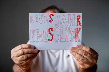 H&auml;nde halten ein wei&szlig;es Schild mit dem handgeschriebenen roten Schriftzug Neues Jahr Neues Gl&uuml;ck vor ein unscharfes Gesicht. Motiv f&uuml;r Optimismus und Neujahrsw&uuml;nsche