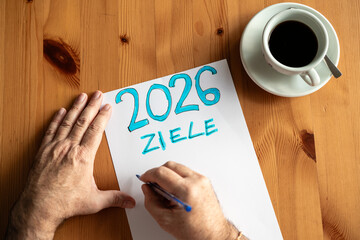 Meine Ziele 2026 H&auml;nde schreiben Neujahrsvors&auml;tze auf Papier, leere Liste f&uuml;r pers&ouml;nliche Planung, Motivation und Neubeginn auf Holztisch
