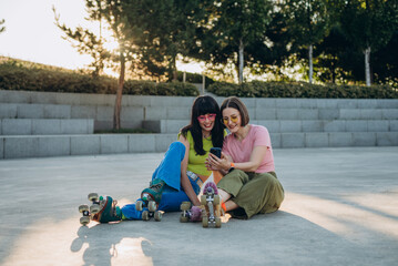 Pretty female friends watch online content of social media on sunset street
