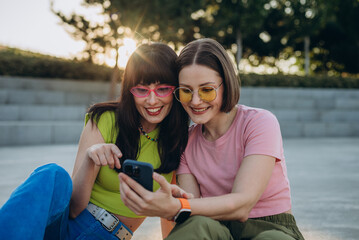 Positive women with stylish eyeglasses scroll internet on smartphone in summer city

