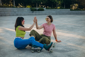Joyful women give high five after a great roller skating in urban park
