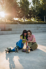 Smiling girl friends scroll social media after roller skating on sunset

